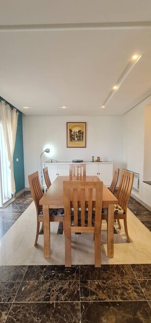 Een eethoek met een rechthoekige tafel en zes stoelen, een keuken op de achtergrond, en een ingelijst schilderij aan de muur.