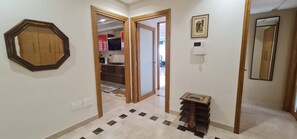 Un pasillo con piso de baldosas, una puerta de madera y una pequeña mesa con libros apilados.