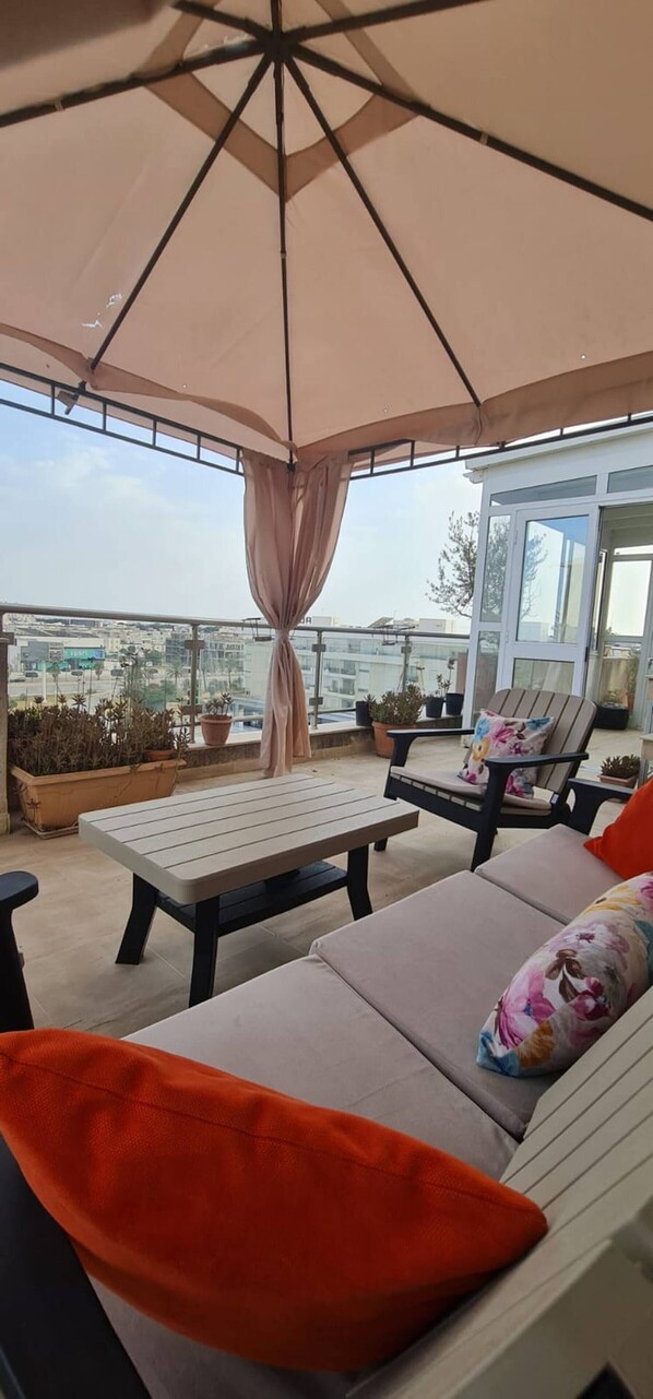 A rooftop terrace with a table and chairs, a large umbrella, and potted plants. - Luxurious 3-bedroom Apartment in Heart of Tunis (Tunis)