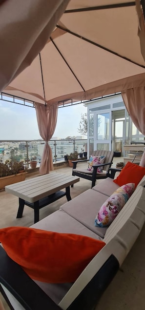 Ein überdachter Außenbereich mit Tisch und Lounge-Stühlen mit Blick auf eine Stadtlandschaft.