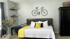 Une chambre avec un lit, une commode, une décoration murale représentant un vélo et une plante en pot.