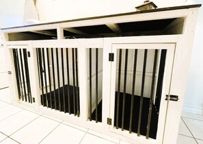 Canil de metal branco com barras verticais e uma porta.