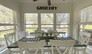 A room with a table and chairs, a ceiling fan, and a window with a sign that reads 'GROCERY'. - Resort-Style 
Backyard Retreat 
Pool-Spa & Firepit (Garden Ridge)