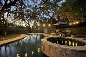 A swimming pool with a stone border, surrounded by trees and outdoor furniture. - Resort-Style 
Backyard Retreat 
Pool-Spa & Firepit (Garden Ridge)