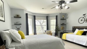 Quarto com uma cama grande, uma cama menor, um ventilador de teto e uma bicicleta na parede.