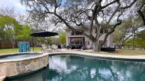 Une piscine bordée de pierres, entourée d’une terrasse aménagée avec des chaises et un parasol.
