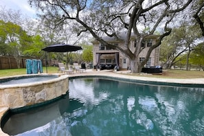 A swimming pool with a stone edge, surrounded by a patio area with chairs and an umbrella. - Resort-Style 
Backyard Retreat 
Pool-Spa & Firepit (Garden Ridge)