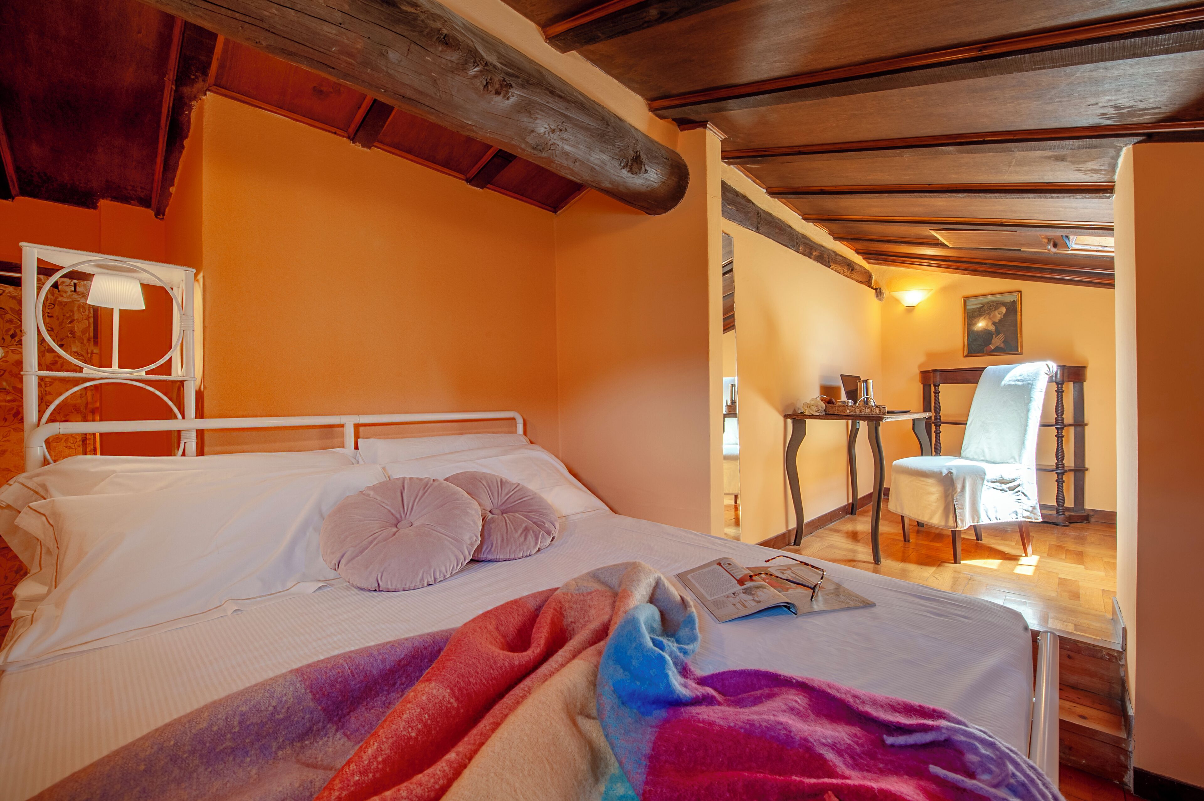 Une chambre à coucher avec un lit, des oreillers, une table de chevet, une chaise et un tableau au mur.