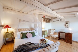 Ein Schlafzimmer mit einem Himmelbett, einem Nachttisch, einem Sessel, einem Schreibtisch und einer Wand-Klimaanlage.