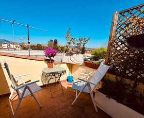 A terrace with two white lounge chairs, a small round table, and a potted plant. - Terrazzino San Frediano - Flo Apartments (Florence)