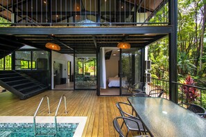 A modern outdoor pool area with a wooden deck, glass balustrades, and a glass table with chairs. - Casa Bamboo, Peaceful 3 bdr Jungle Home in Uvita, 2min from river and waterfalls (Uvita)