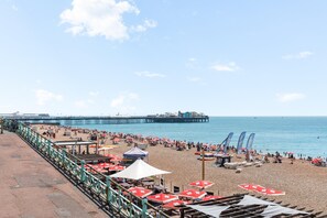 A beach with umbrellas, chairs, and a pier in the background. - Kings Residence 8 | By My Getaways (Brighton)