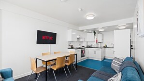Moderni olohuone, jossa on ruokailutila, pieni keittiö sekä kuviollisilla tyynyillä varustettu sohva.