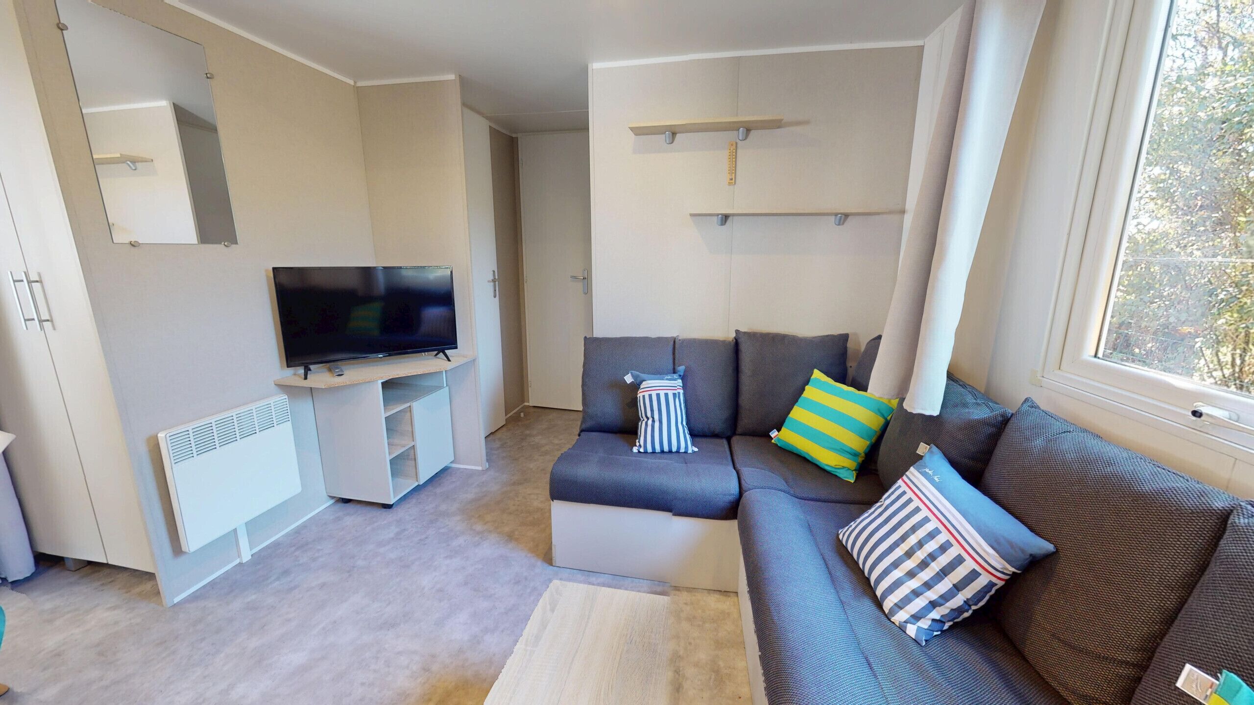 A modern living room with a flat-screen TV, a sofa set, and a window with curtains.