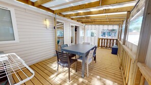 A covered outdoor area with a table and chairs, wooden flooring, and a view of the outside. - Sun & Pool: 3-bedroom mobile home, patio & pool (Saint-Hilaire-de-Riez)