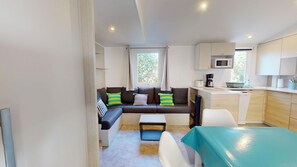 A compact living space with a sofa, a small dining table, and a kitchenette. - Sun & Pool: 3-bedroom mobile home, patio & pool (Saint-Hilaire-de-Riez)