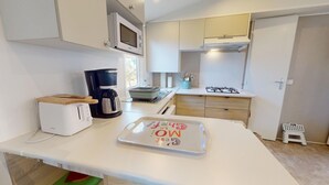 A compact kitchen with a toaster, coffee maker, microwave, and a small gas stove. - Sun & Pool: 3-bedroom mobile home, patio & pool (Saint-Hilaire-de-Riez)