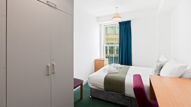 A hotel room with a bed, a desk, a wardrobe, and a window with curtains. - Kings Residence 2 | By My Getaways (Brighton)