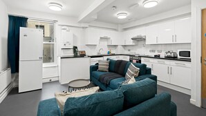 A modern kitchen with white cabinets, a dining area with a teal sofa, and a small round table. - Kings Residence 2 | By My Getaways (Brighton)
