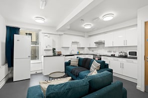 Eine moderne Küche mit weißen Schränken, ein Essbereich mit einem blaugrünen Sofa und einem kleinen runden Tisch.
