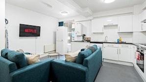 A modern kitchen with white cabinets, a built-in oven, and a sink. There is a flat-screen TV mounted on the wall displaying 'NETFLIX'. - Kings Residence 2 | By My Getaways (Brighton)