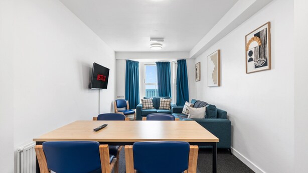 Ein modernes Wohnzimmer mit einem Holztisch, blauen Stühlen, einem blauen Sofa und einem an der Wand befestigten Fernseher.