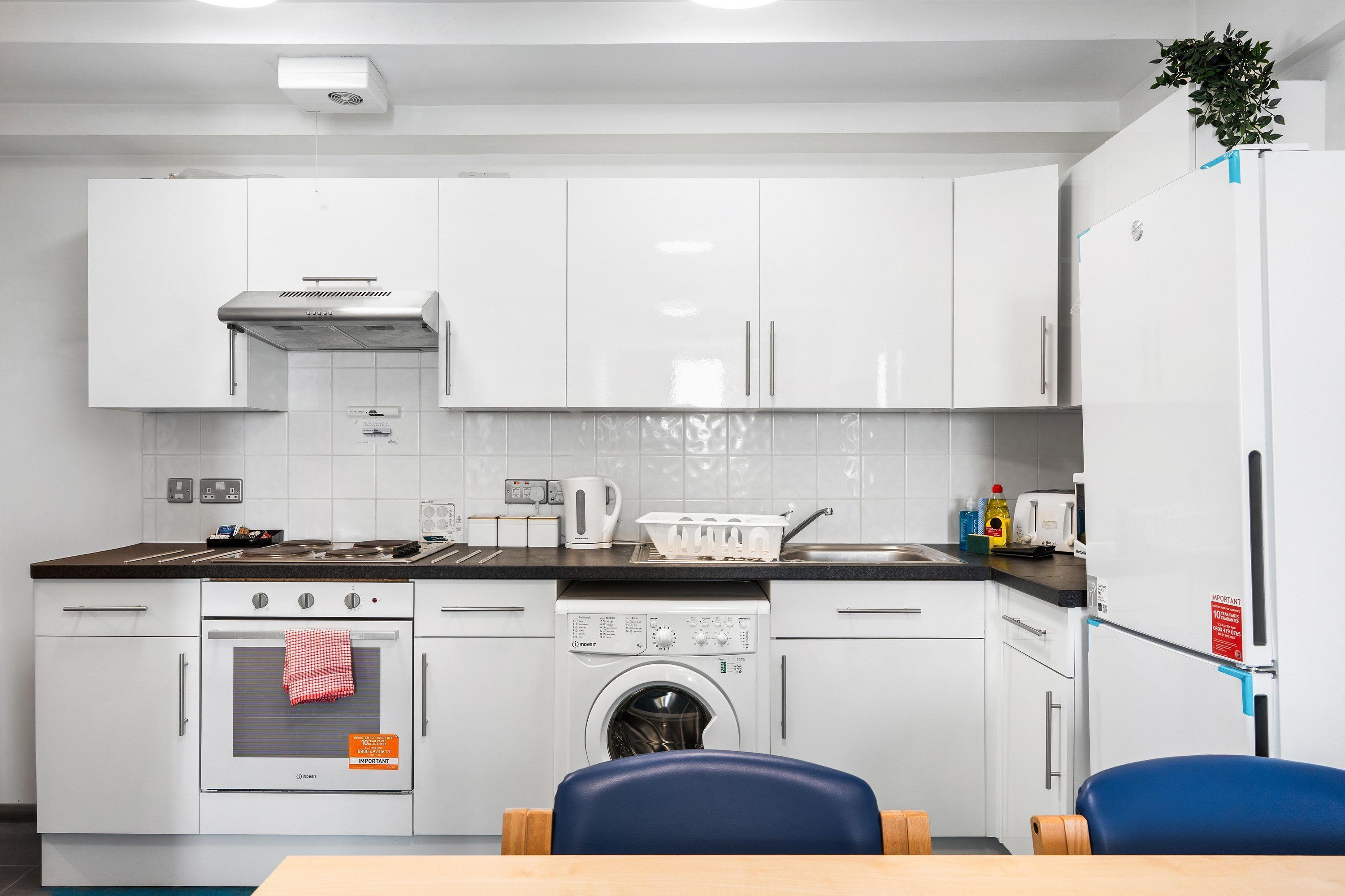 A modern kitchen with white cabinets, a built-in oven, a washing machine, and a refrigerator.