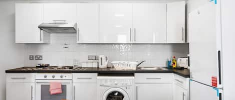 A modern kitchen with white cabinets, a built-in oven, a washing machine, and a refrigerator.