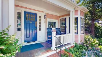 A house with a blue front door, a porch with two chairs, and a brick foundation.