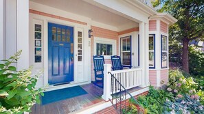 A house with a blue front door, a porch with two chairs, and a brick foundation.