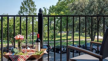 Un balcon avec une table dressée pour un repas, une bouteille de vin et un vase de fleurs.