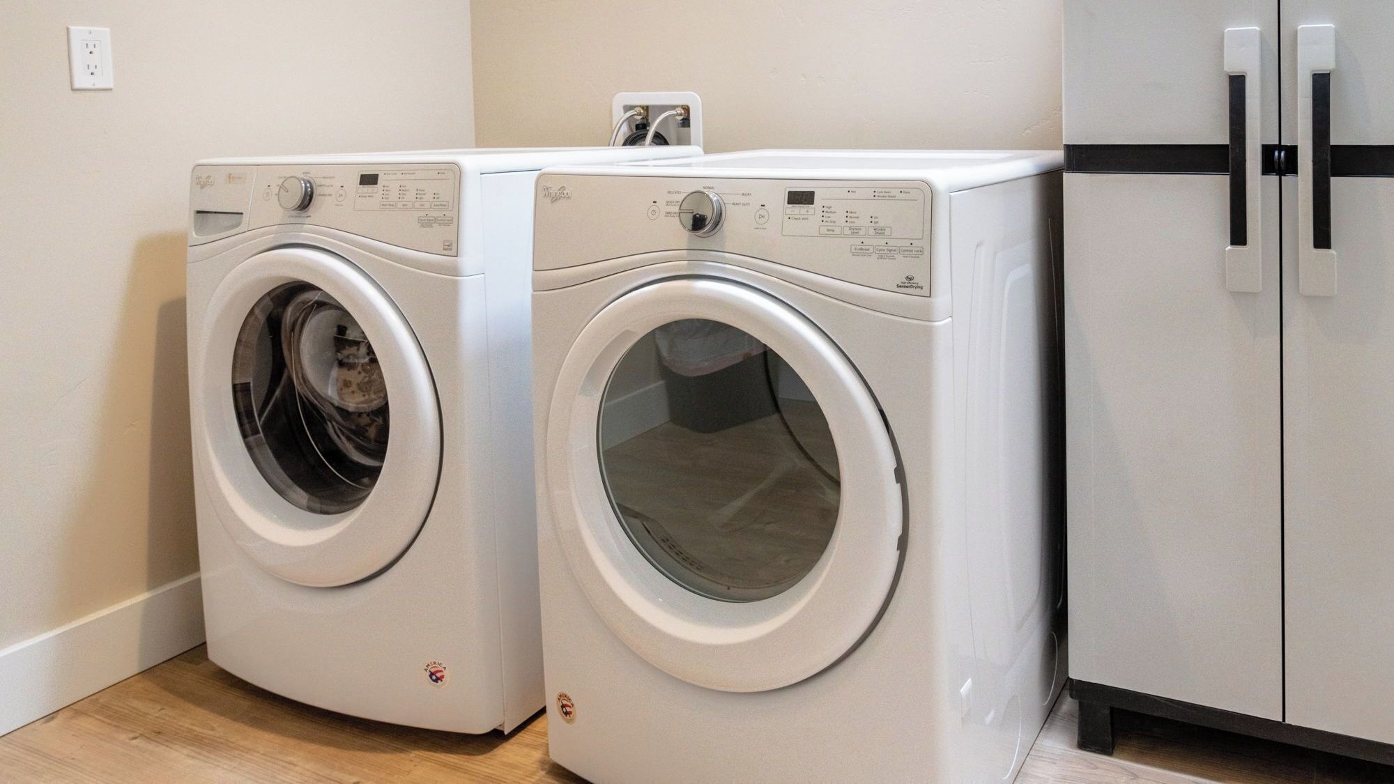 Two front-loading washing machines in a laundry room with a refrigerator.