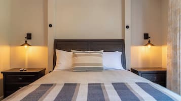 Un lit avec une couverture à rayures, deux tables de chevet avec des lampes et une tête de lit en bois foncé.