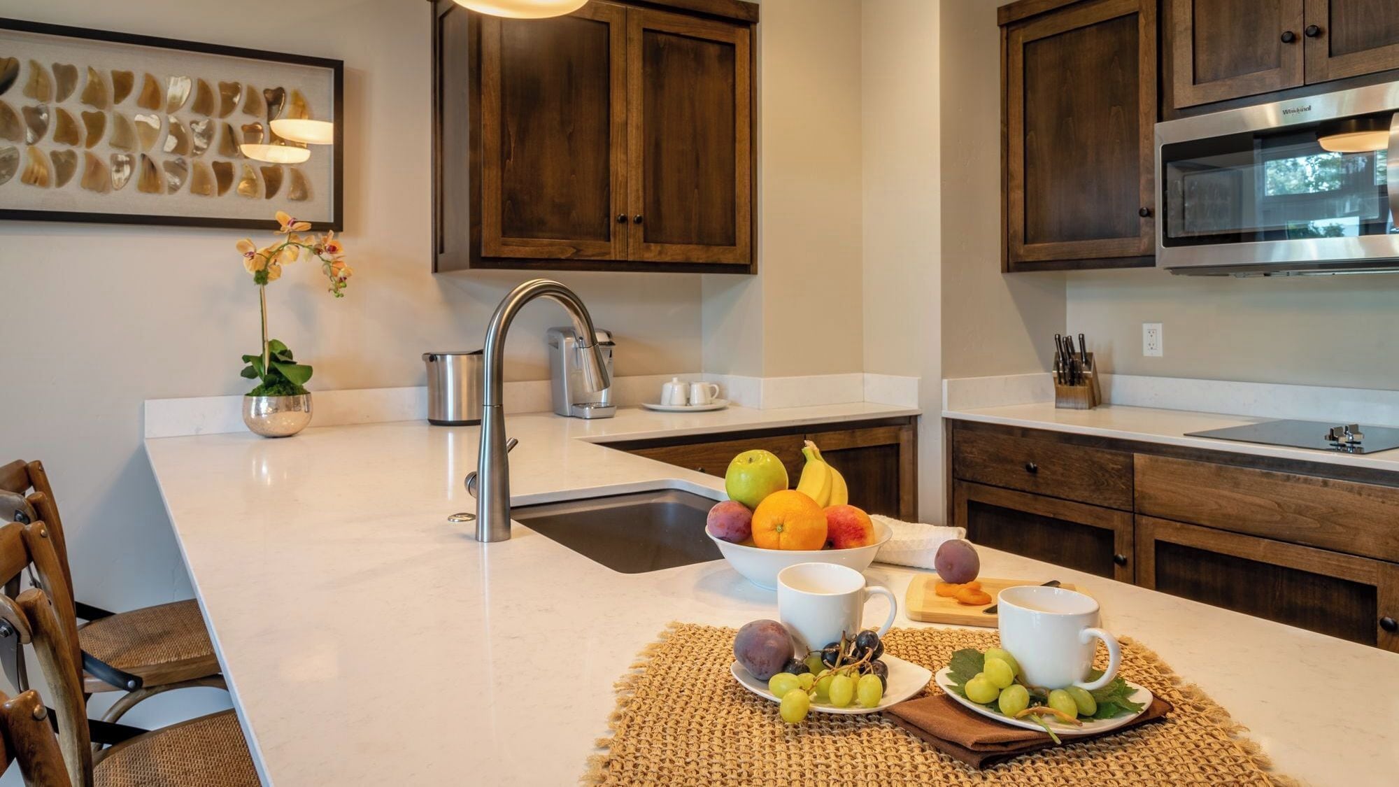 A modern kitchen with a white countertop, stainless steel sink, and wooden cabinets.