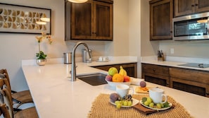A modern kitchen with a white countertop, stainless steel sink, and wooden cabinets. - Paso Park Suites by Avantstay 2 Private Balconies + Town Square Views Downtown Paso Robles (Paso Robles)