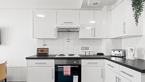 A modern kitchen with white cabinetry, a built-in oven, a stove, and a coffee maker. - Kings Residence 4 | By My Getaways (Brighton)
