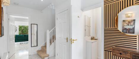 A hallway with a staircase, a white door, and a mirror.