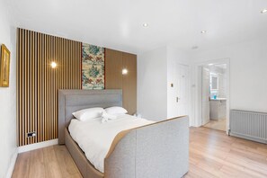 A modern bedroom with a large bed, wooden panel wall, and a view into the bathroom. - Downs Heights | By My Getaways (Brighton)