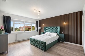 A bedroom with a large bed, a window, a radiator, and a wooden wall panel. - Downs Heights | By My Getaways (Brighton)