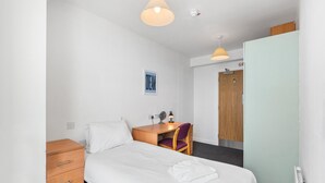 Ein Hotelzimmer mit Bett, Schreibtisch, Stuhl, Kleiderschrank und einer Deckenleuchte.
