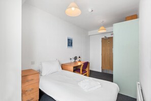 Ett hotellrum med en säng, ett skrivbord, en stol, en garderob och en taklampa.