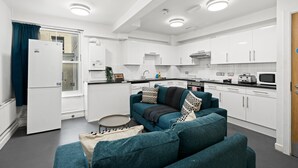 Eine moderne Küche mit weißen Schränken, ein Essbereich mit einem türkisgrünen Sofa und einem kleinen runden Tisch.