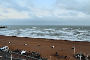 A beach with a pier in the distance, a sandy shore, and a building with a roof. - Kings Residence 5 | By My Getaways (Brighton)
