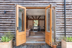 A wooden cabin entrance with a door open, revealing a dining area with a table and chairs, and a window with a view of greenery. - Medleys Barn | By My Getaways (High Hurstwood)