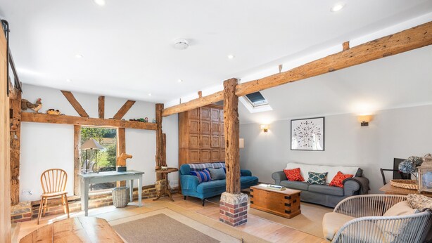 A spacious living area with exposed wooden beams, a blue sofa, a wooden coffee table, and a wicker chair. - Medleys Barn | By My Getaways (High Hurstwood)