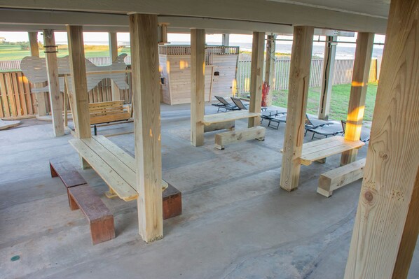 A covered outdoor area with wooden benches and picnic tables, a wooden deck, and a view of the beach.