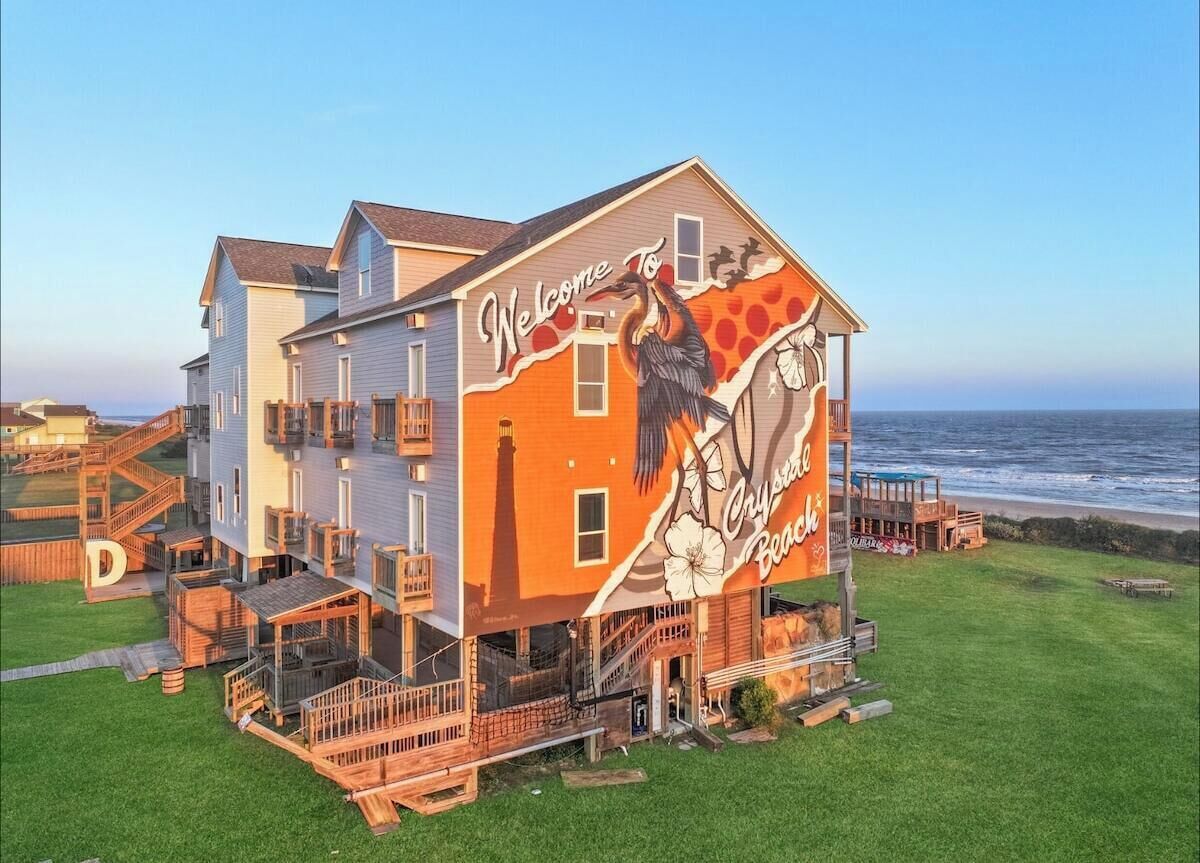 A multi-story building with a large mural on the side, a wooden deck, and a view of the ocean.