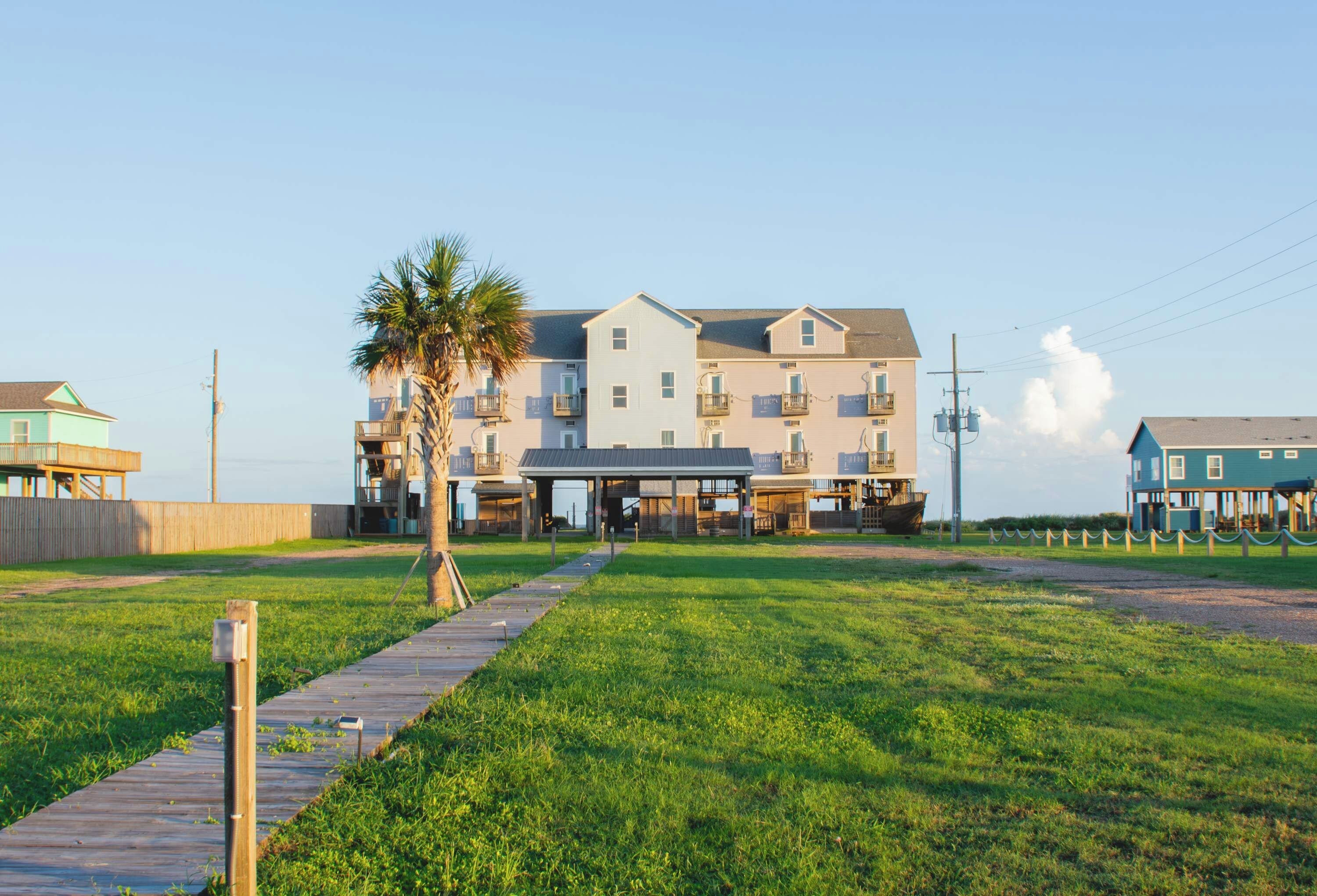 A beachfront hotel with multiple floors, a covered walkway, and a palm tree.