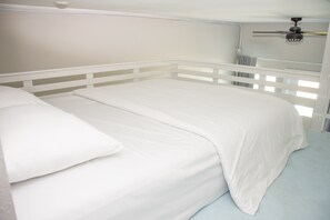 A bed with white bedding in a room with a white headboard and a ceiling fan.