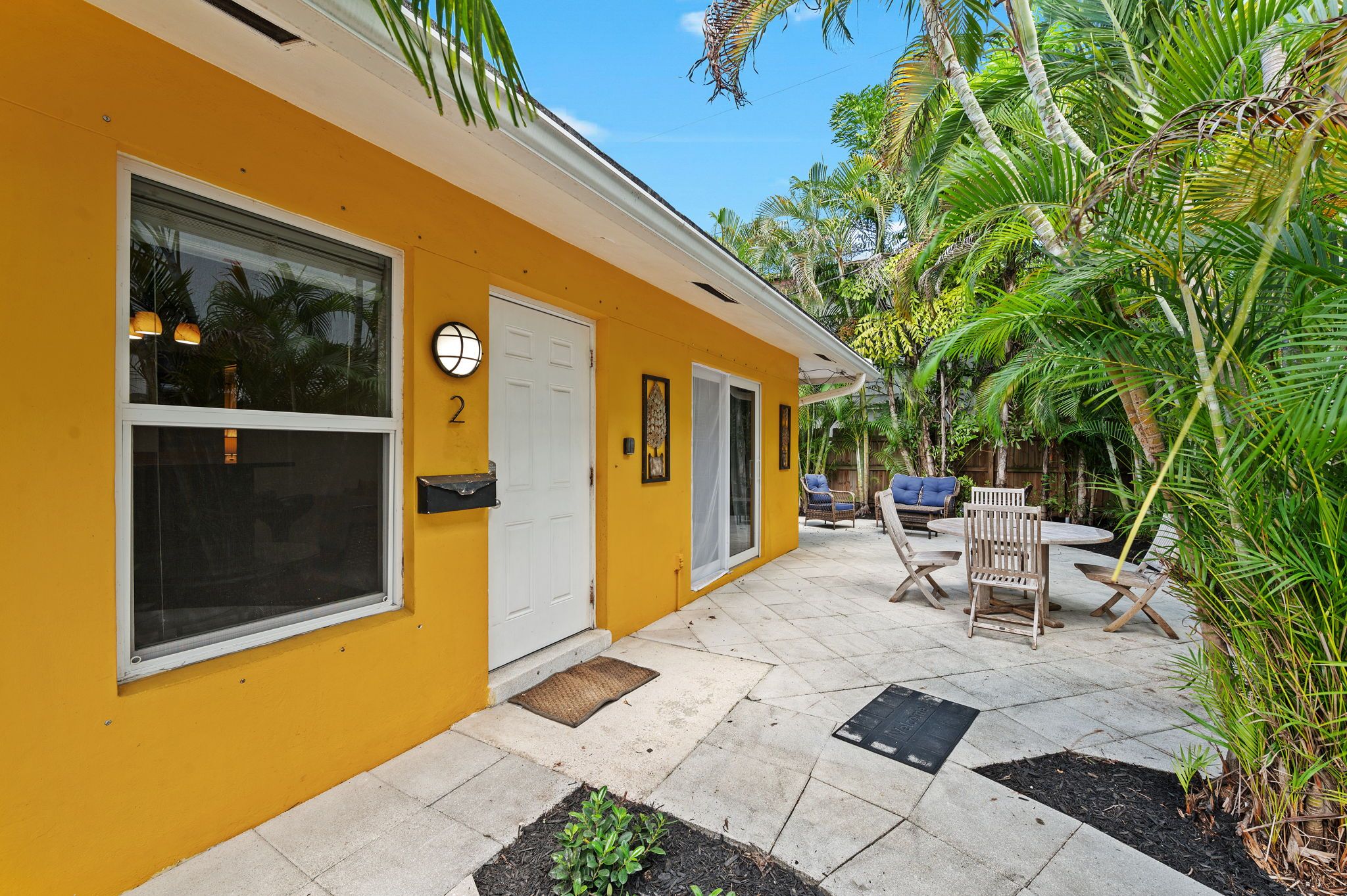 A yellow building with a covered patio area, outdoor seating, and a door marked with the number 2.